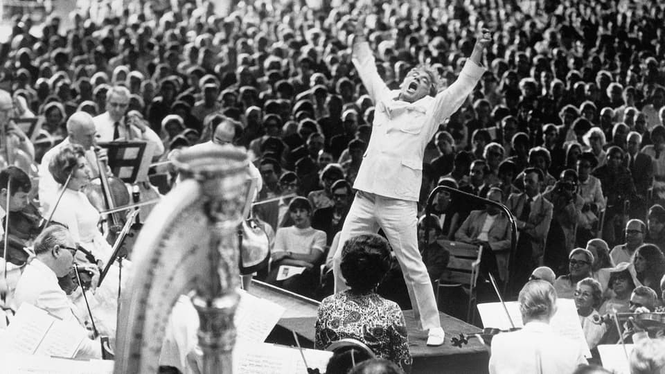 A conductor leading an orchestra in front of a packed audience